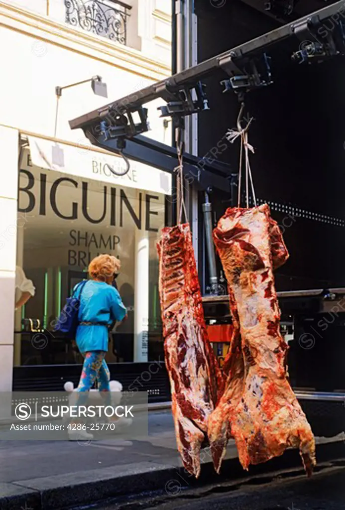 Parisian woman walking her French poodle past two butchered carcases