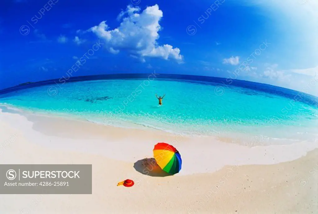 Woman alone in paradise with parasol and hat on beach