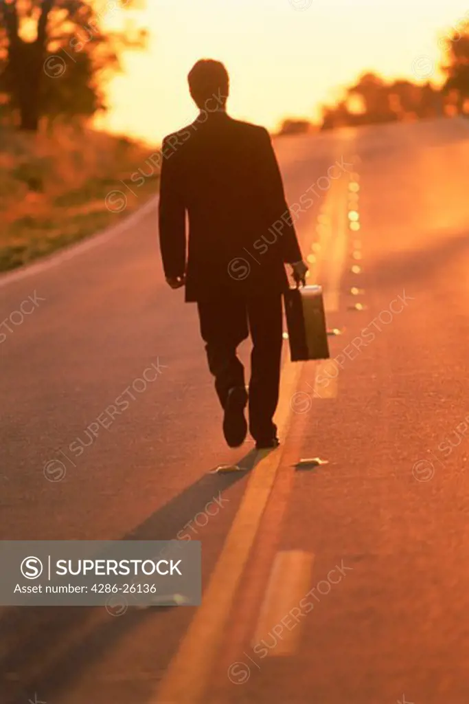 Businessman with briefcase walking endless highway at dawn