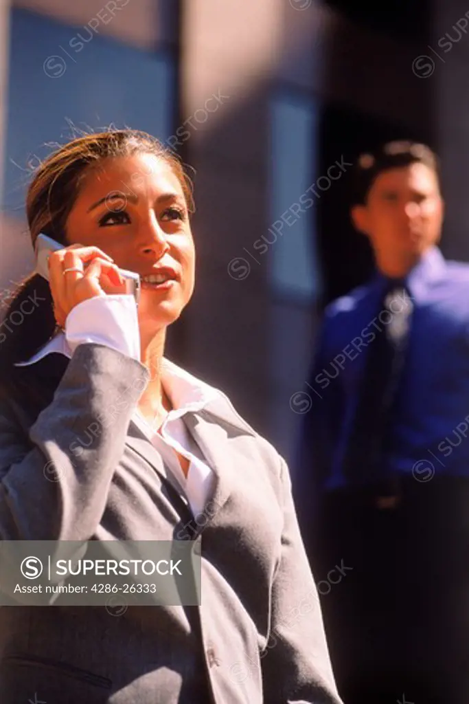 Businesswoman talking on cellphone with man behind