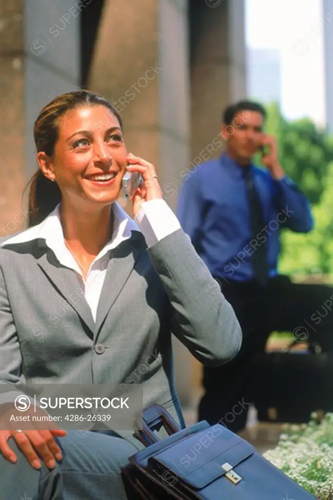 Hispanic businesswoman talking on cellphone with man behind