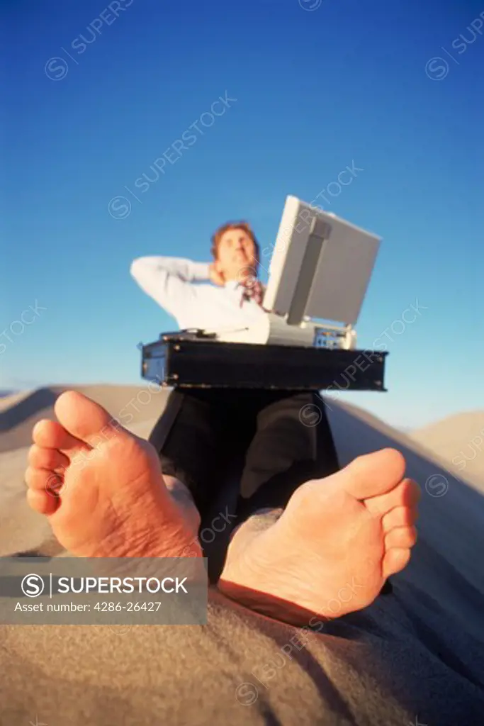Barefoot businessman using desert sand for outdoor office space