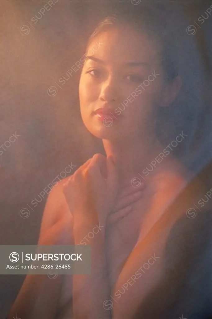 Asian Caucasion woman nude behind curtain in soft bedroom light