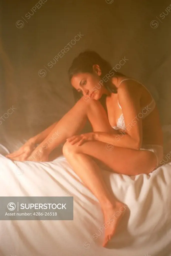 Latino woman in white lengerie behind curtain in soft bedroom light