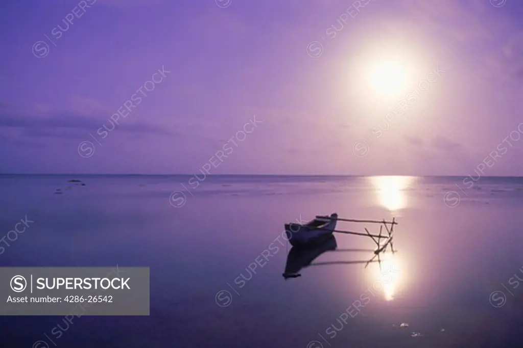Outrigger in calm lagoon off Aitutaki Island under full moon in South Pacific
