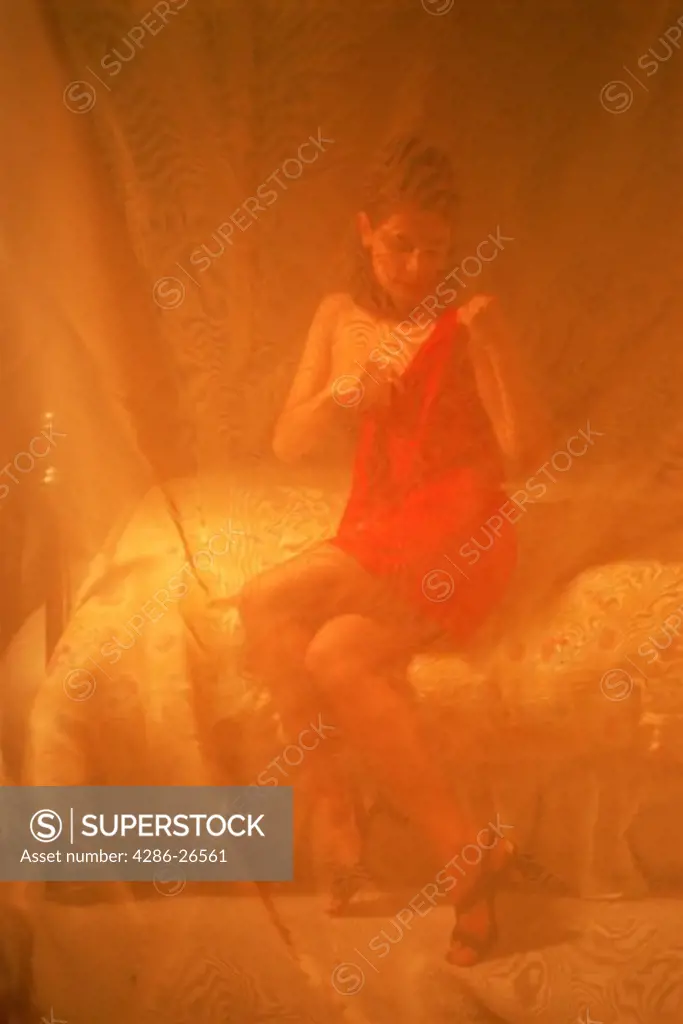 Woman putting red dress on in soft bedroom light