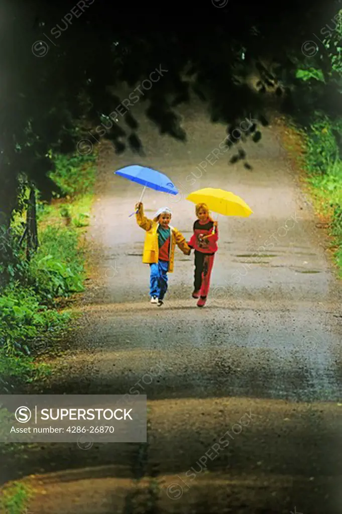 Boy and girl running on country road in the rain holding umbrellas