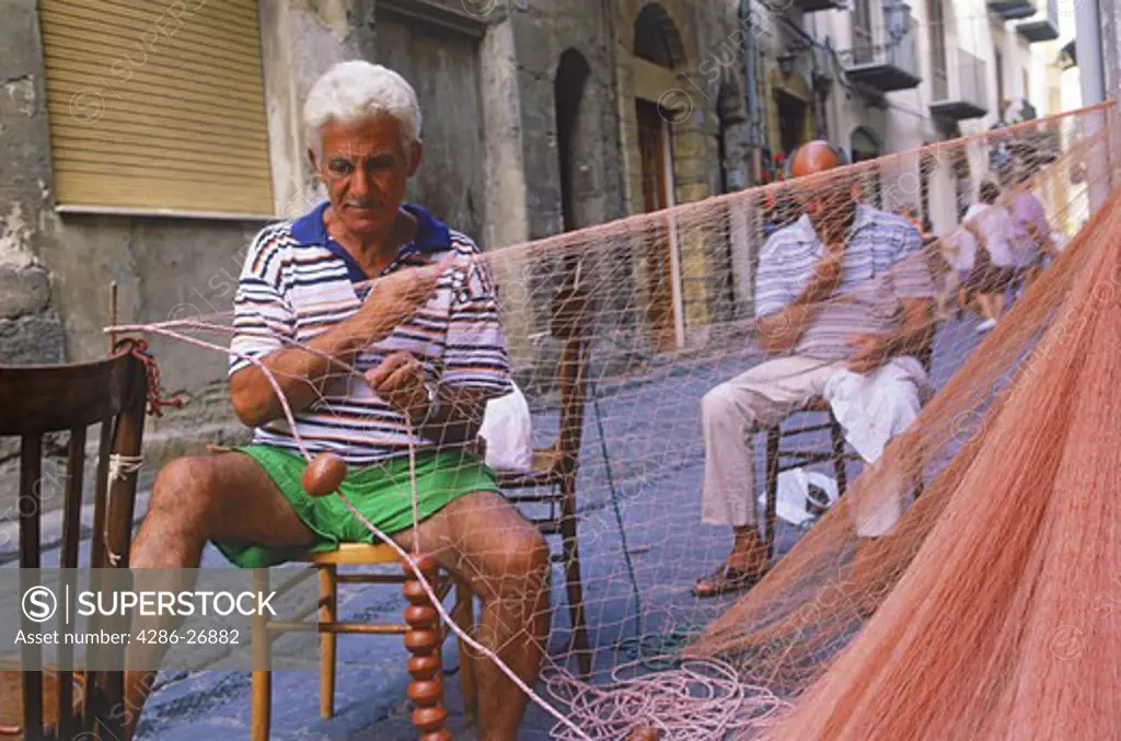Men repairing fish nets in village of Cefalu on Sicily