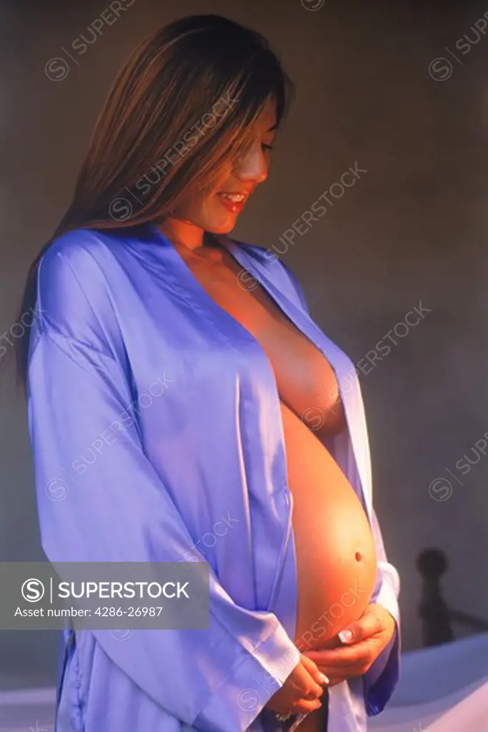 Woman in 8th month of pregnancy in soft bedroom light