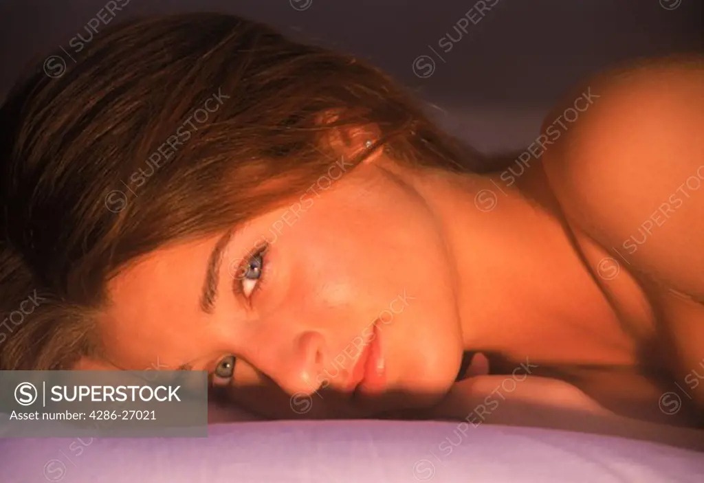 Young woman lying on bed in thoughtful pose