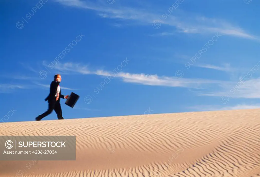 Businessman in suit with briefcase racing up sand dune