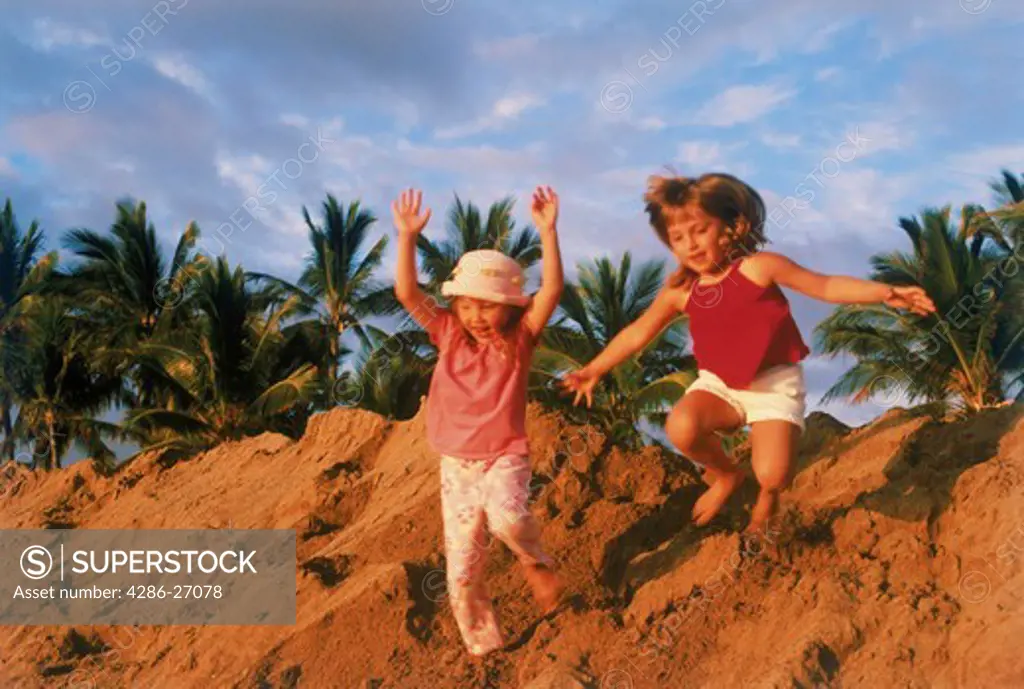 Two girls jumping off sandy hill in sunset light