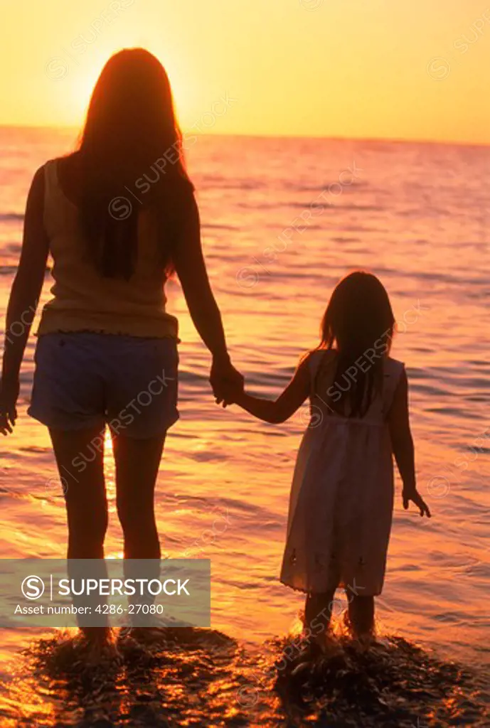 Mother and daughter holding hands on beach in sunset light
