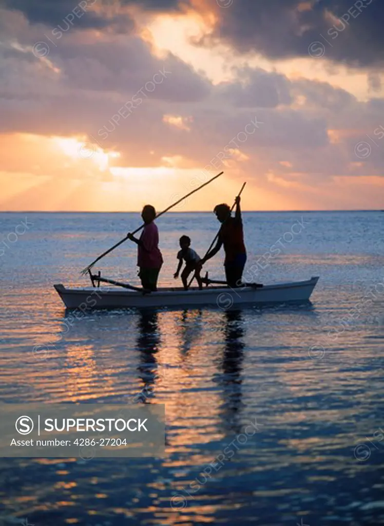Family in outrigger canoe spearfishing on Aitutaki lagoon at sunset