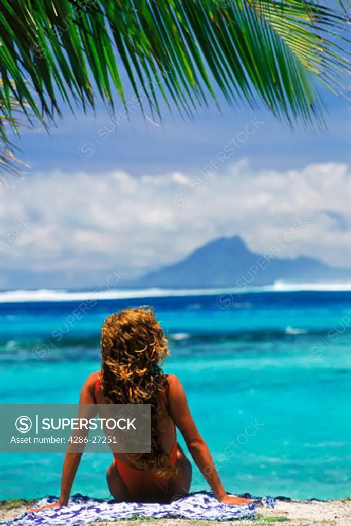 Woman sitting on Huahine Island beach with Raitea Island beyond in French Polynesia