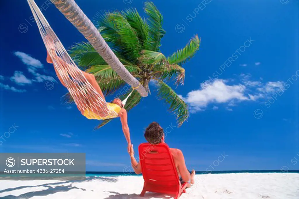 Couple chilling out under hanging palm tree and sunny skies on white sands in Maldives