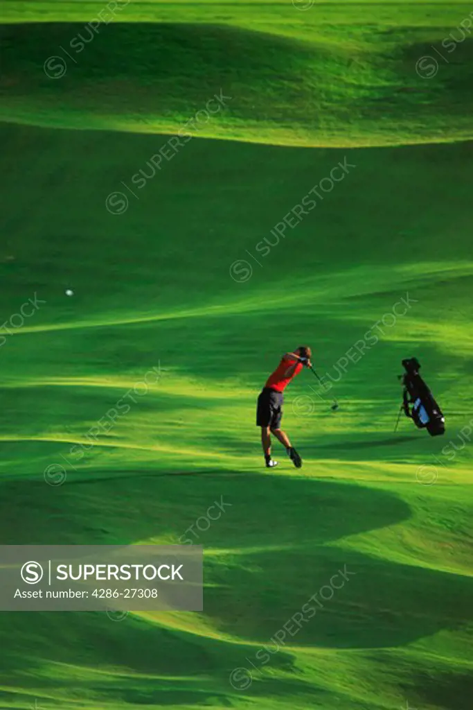 Male golfer hitting iron shot off lush green fairway in low light