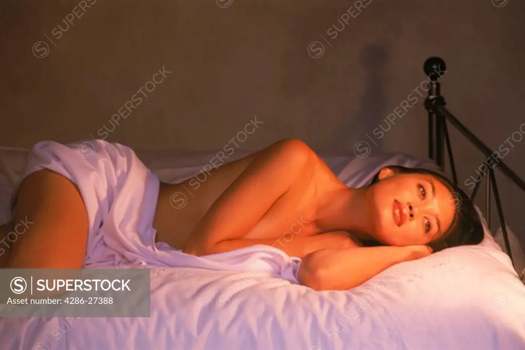 Woman of ethnic mix resting semi nude on bed in soft lamplight