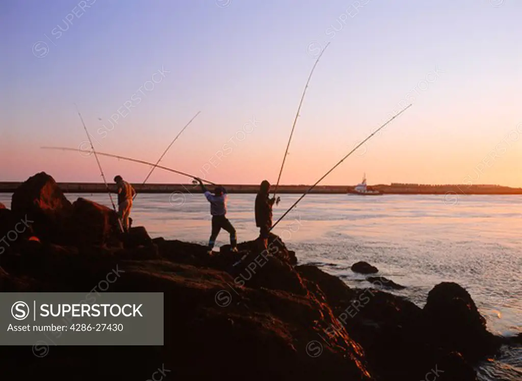 People fishing off rocks near Aveiro harbour at sunset Portugal