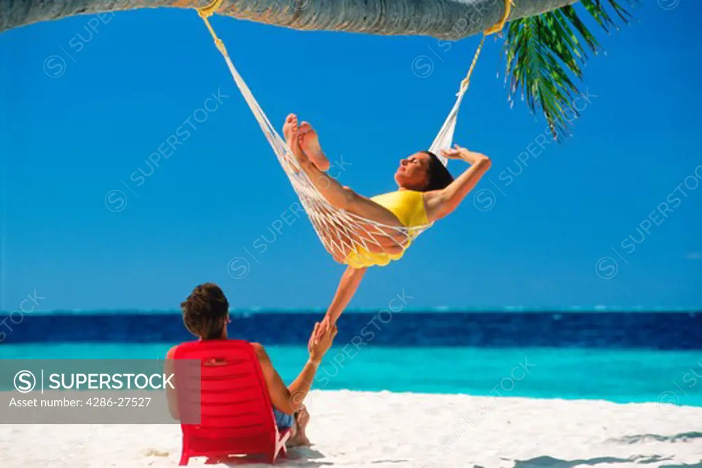 Man in chair and woman in hammock on relaxing holiday