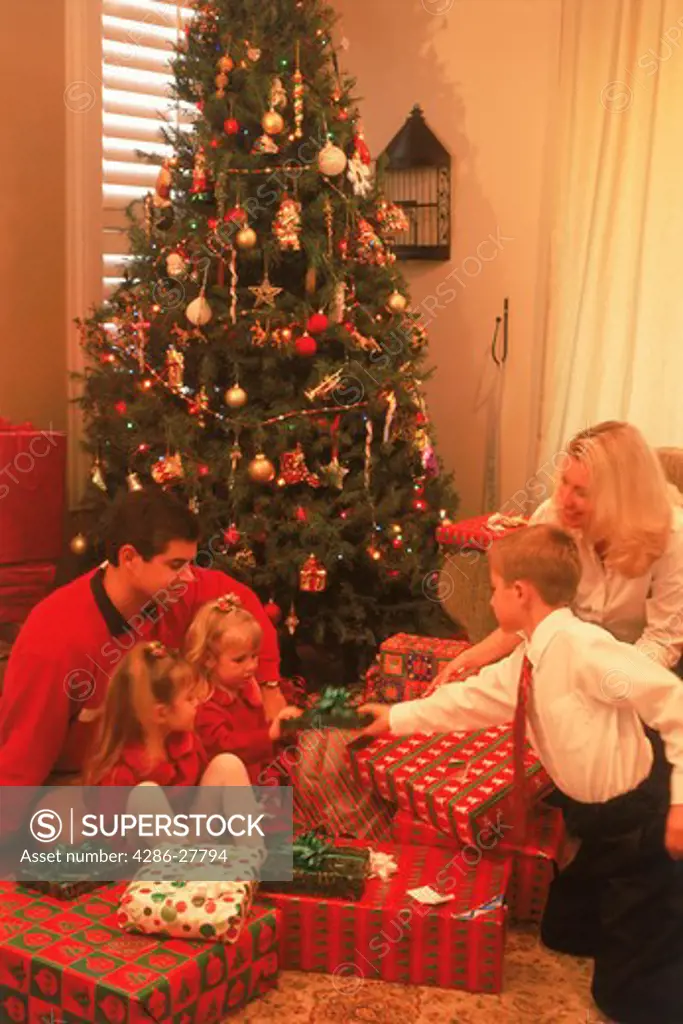 Family of five around home Christmas tree sharing presents