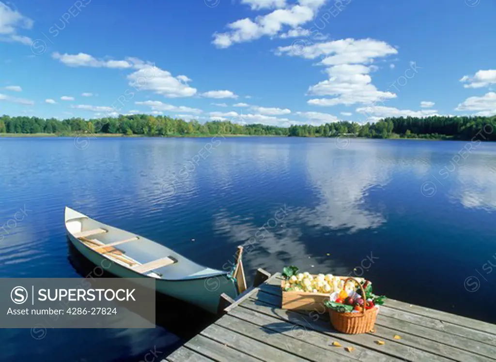 Crate of apples and basket of mixed vegetables on lake pier with canoe in Sweden near Flen