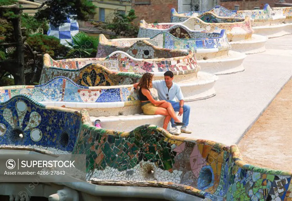 Couple sitting on bench of mosaic artwork by Antonio Gaudi at Guell Park in Barcelona, Spain
