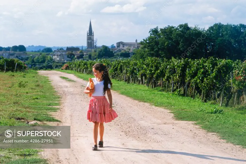 Girl walking through vineyards with baguettes near village of St Emilion in France