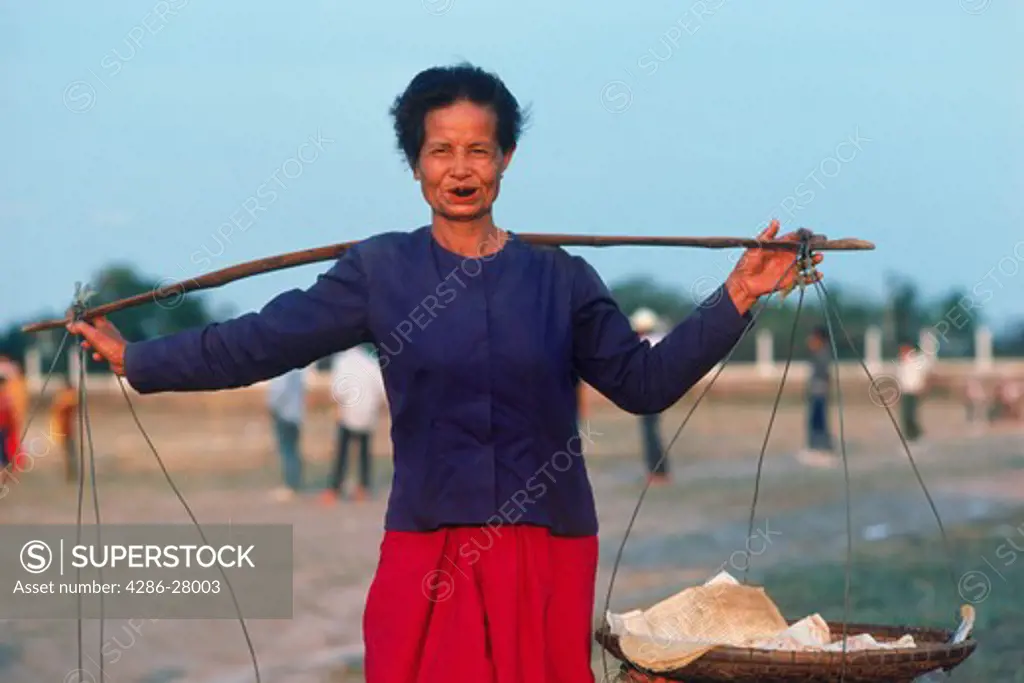 Thai woman carrying load on shoulder pole while chewing betel nut