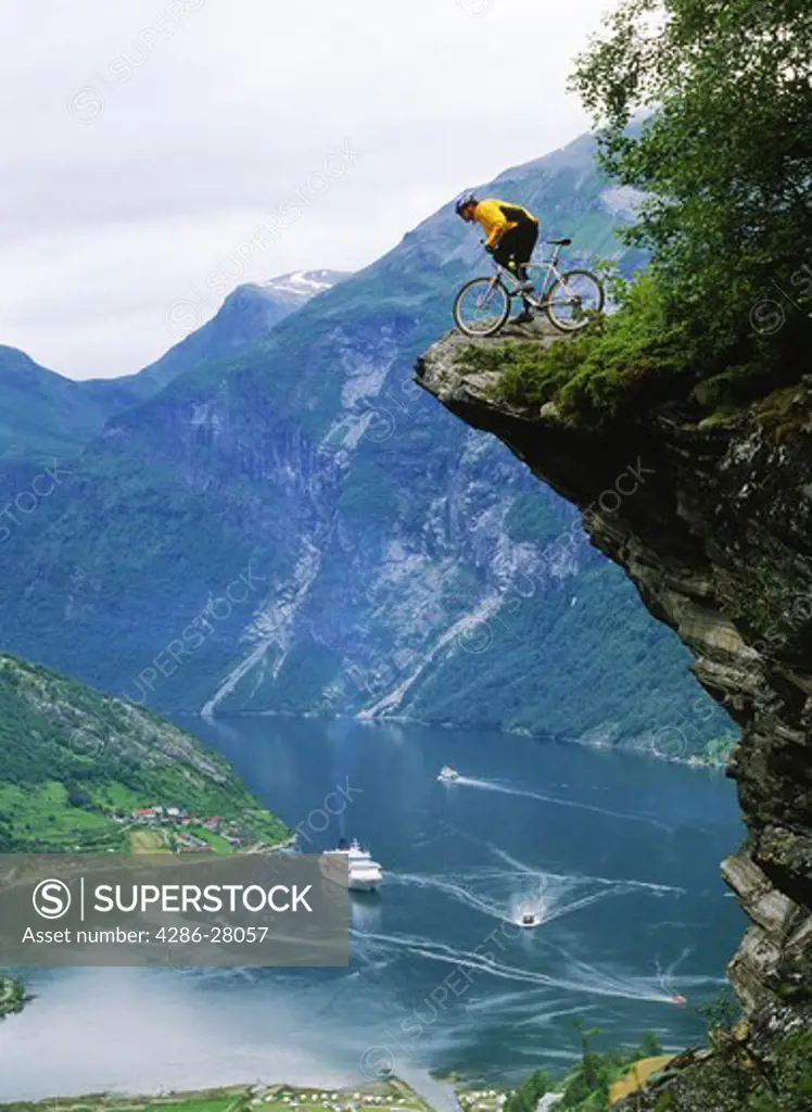 Mountain biker at Flydalsjuvet above Geiranger Fjord with cruise ship on Norwegian coast