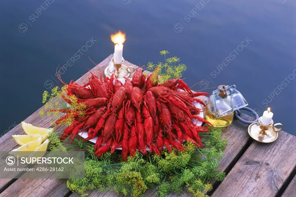 Bowl of crayfish on lakeside pier with candles and aquavit in Sweden