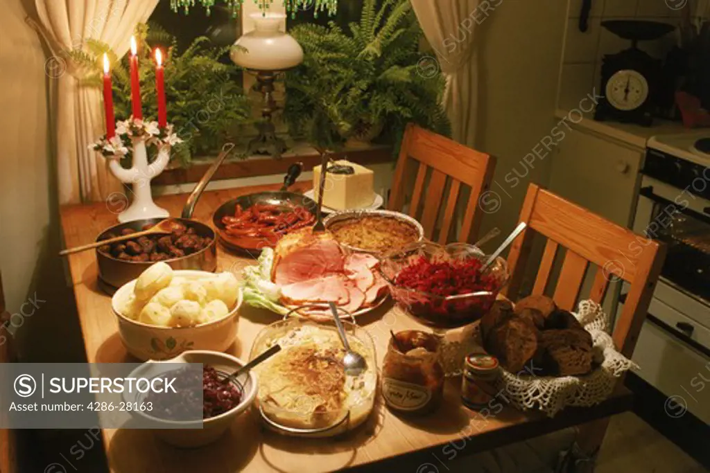 Swedish Christmas table or julbord with cheese, potatoes, beets, meatballs, baked bread, roast ham, marinated herring and candle