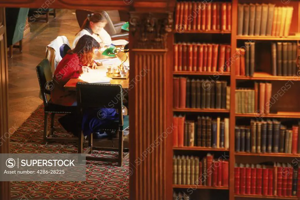 Two students in school library with workbooks and pens under lamplight