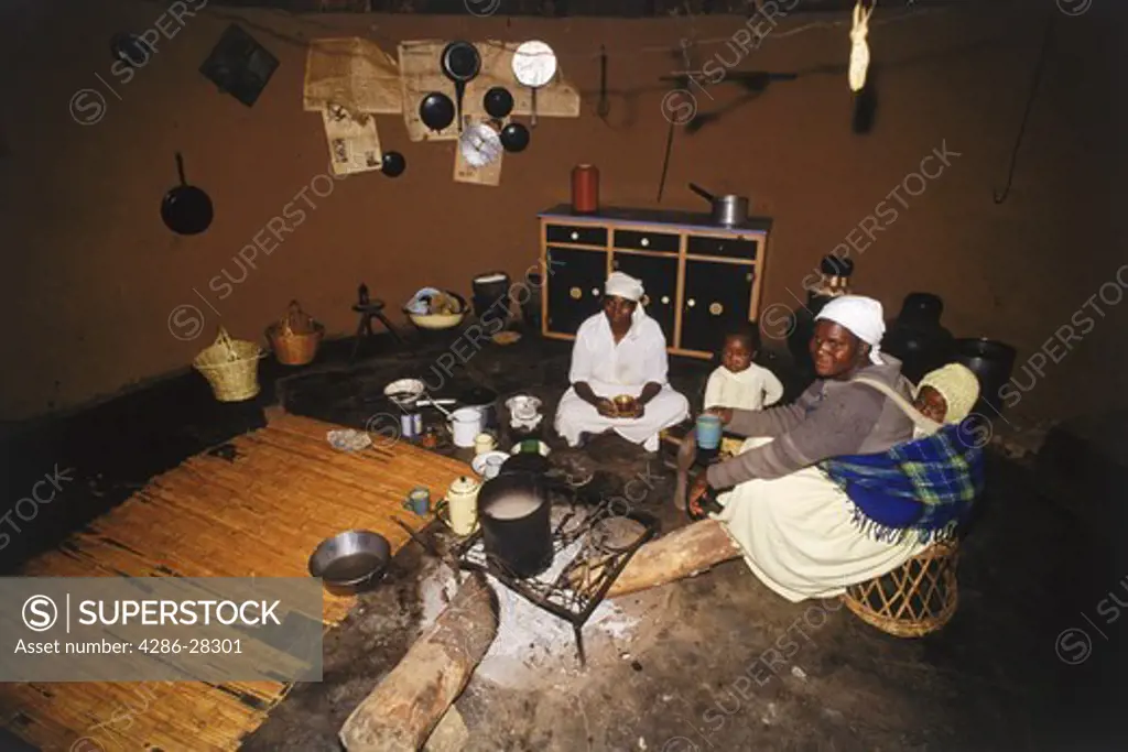 Mothers with their children cooking food in basic African village hut in Zimbabwe