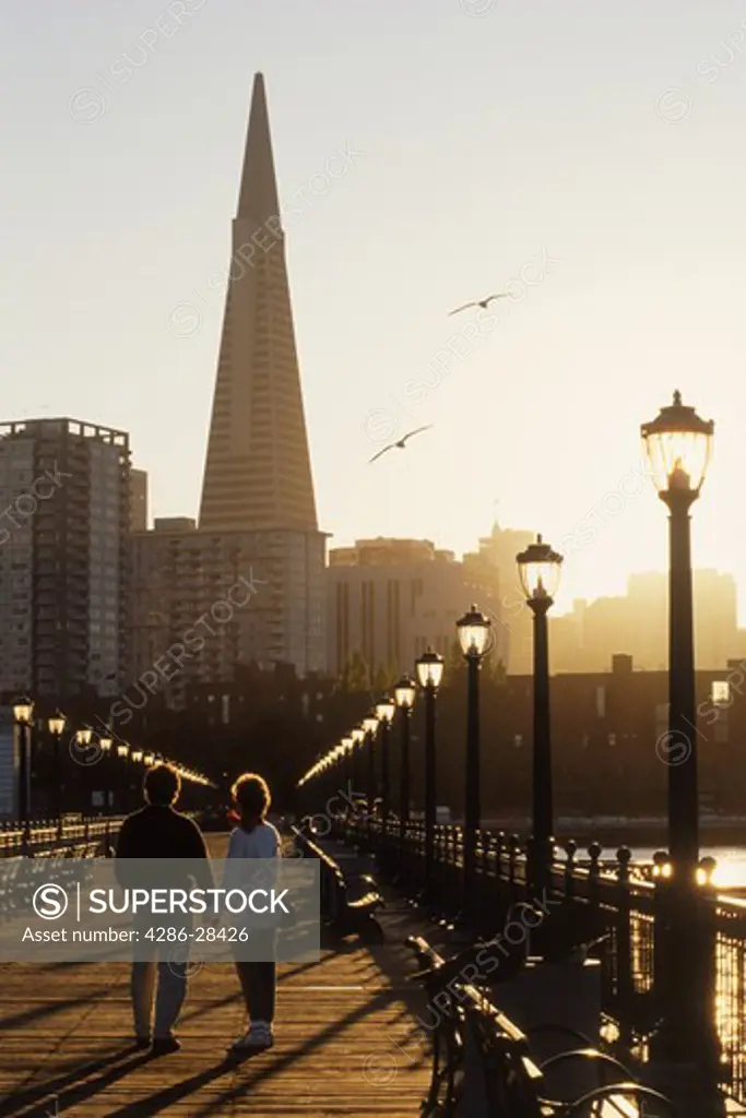 Couple on Pier 7 under lamps and seagulls and San Francisco skyline with TransAmerica building  at sunset