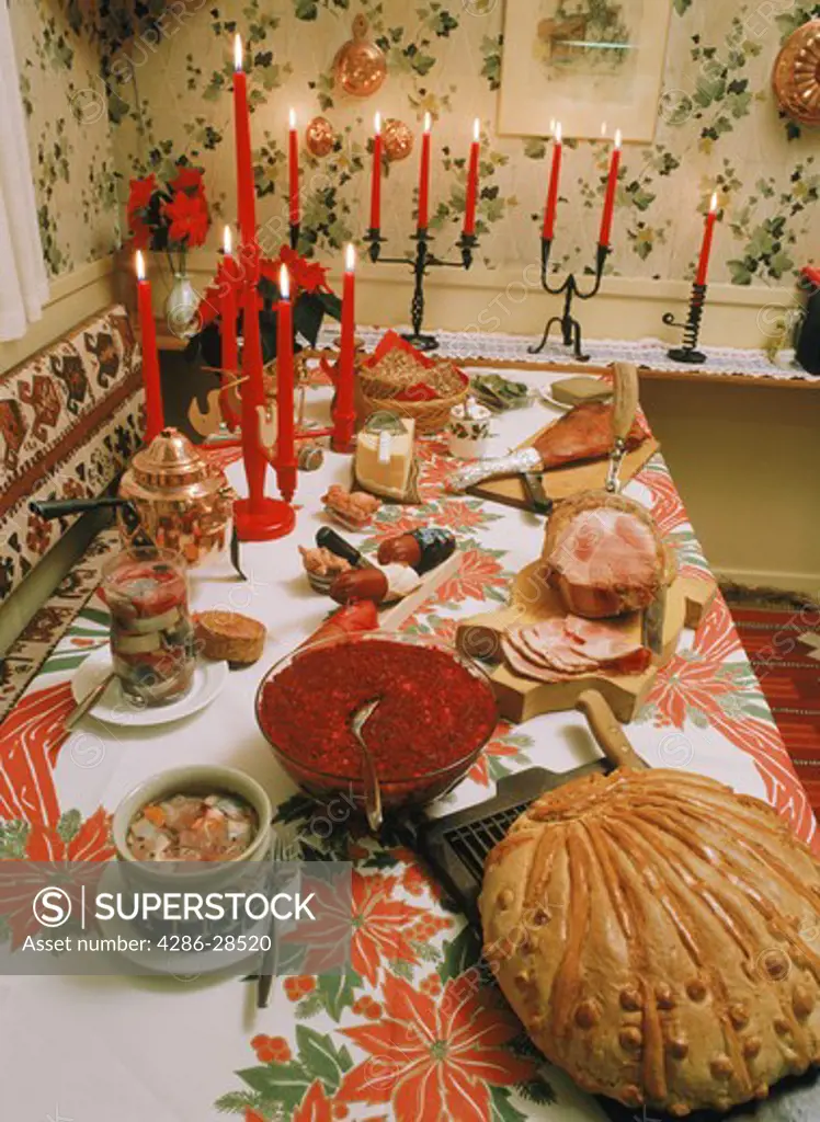 Swedish Christmas table or julbord with cheese, baked bread, beats, aquavit, roast ham, marinated herring and candles