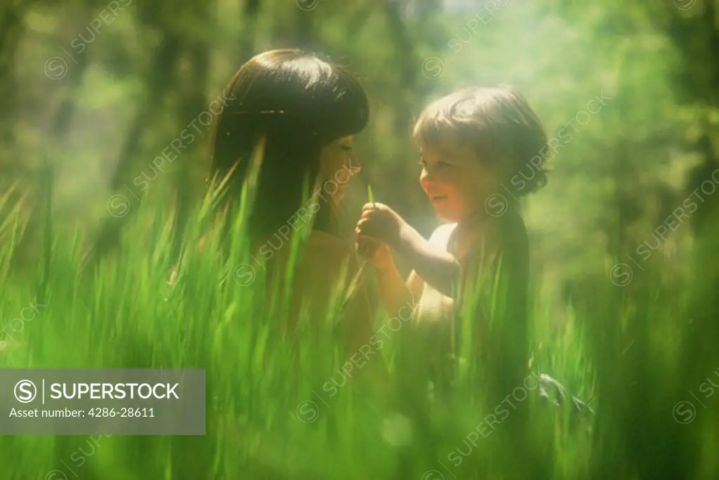 Mother and son sitting in field of sunlit green grass