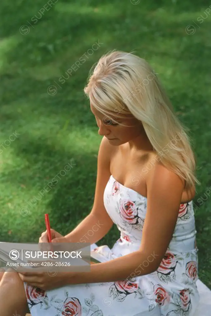 Young lady reading and writing outside in summer dress