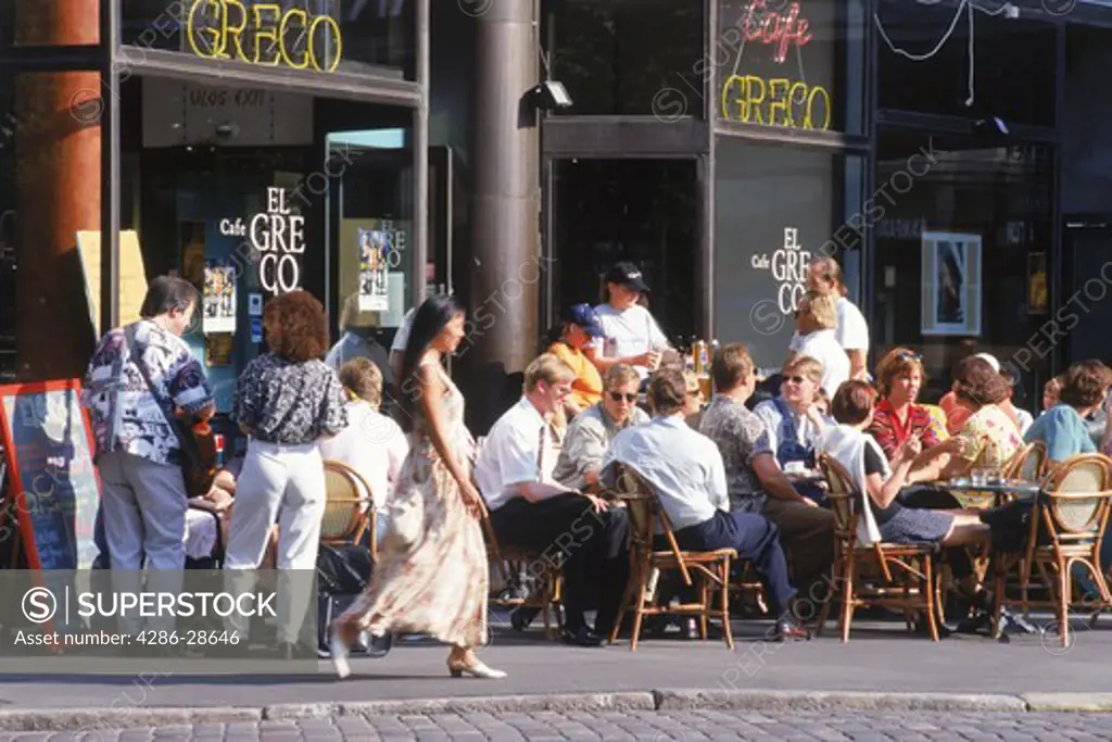 Woman in summer dress passing sidewalk cafe and coffee shop in Helsinki, Finland