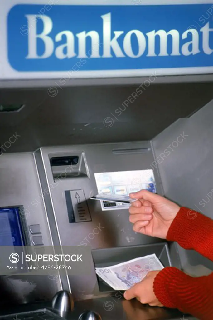 Hands holding money and debit card at ATM machine in Sweden