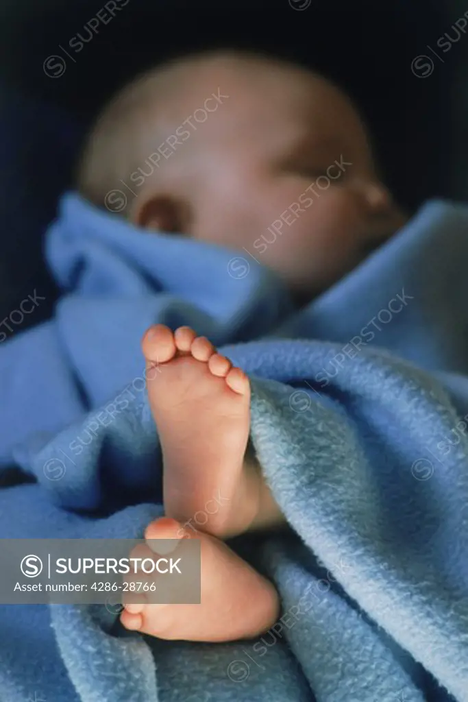 Feet of baby 3 to 6 months old peeking from under blue blanket
