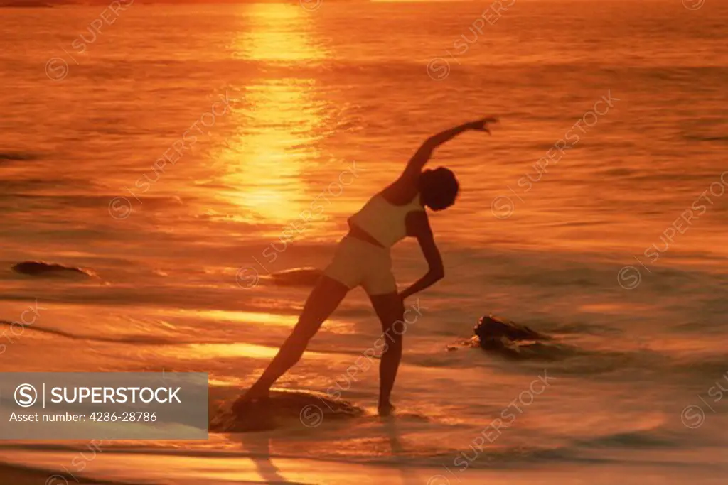 Woman in yoga position on shore at sunset