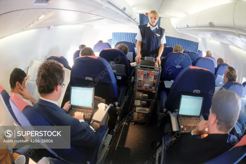 Inflight passengers using laptops with stewardess and duty free cart