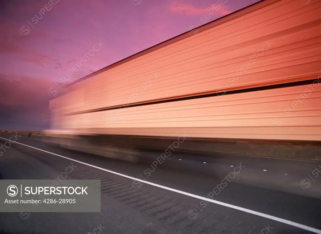 Truck and trailer speeding along California highway reflecting sunset light