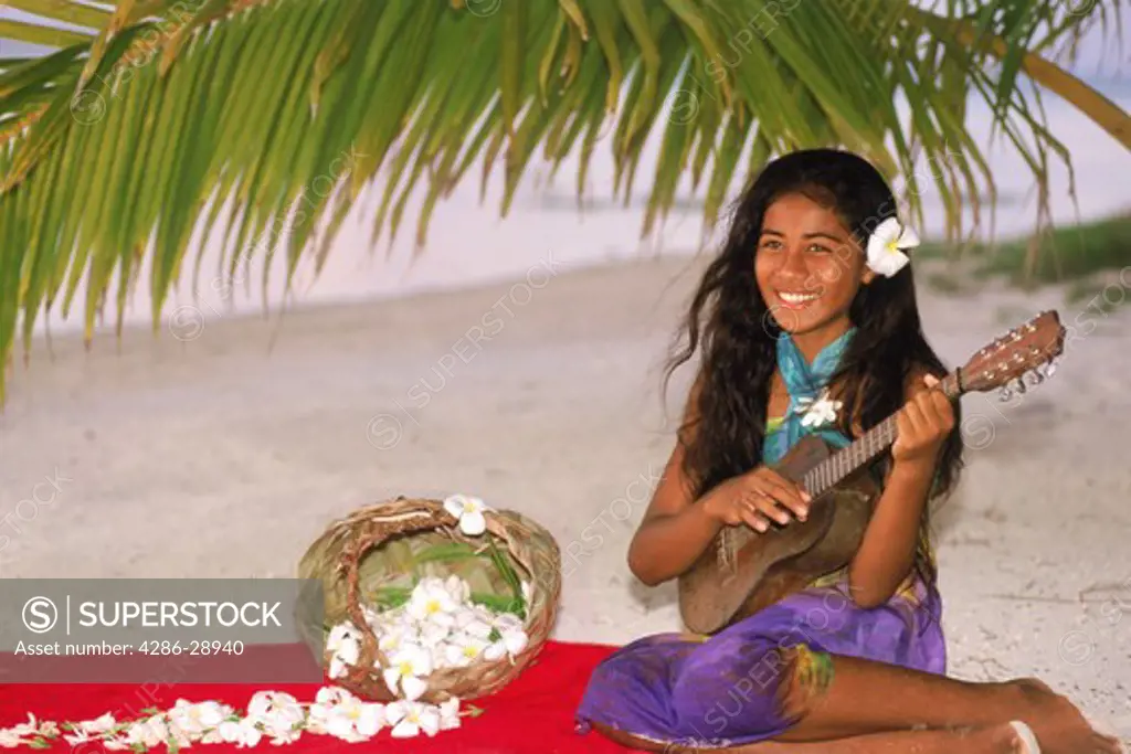 Polynesian girl sitting on Aitutaki beach under plam frond playing ukelele