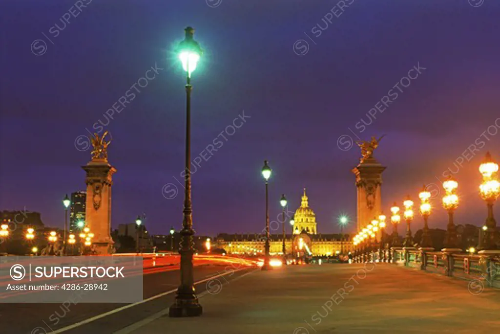 Pont Alexandre III traffic with lamplights and Hotel des Invalides at night in Paris