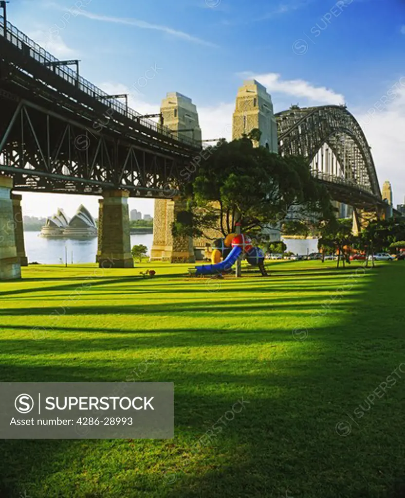 Morning light across grassy park under Harbour Bridge in North Sydney opposite the Opera House
