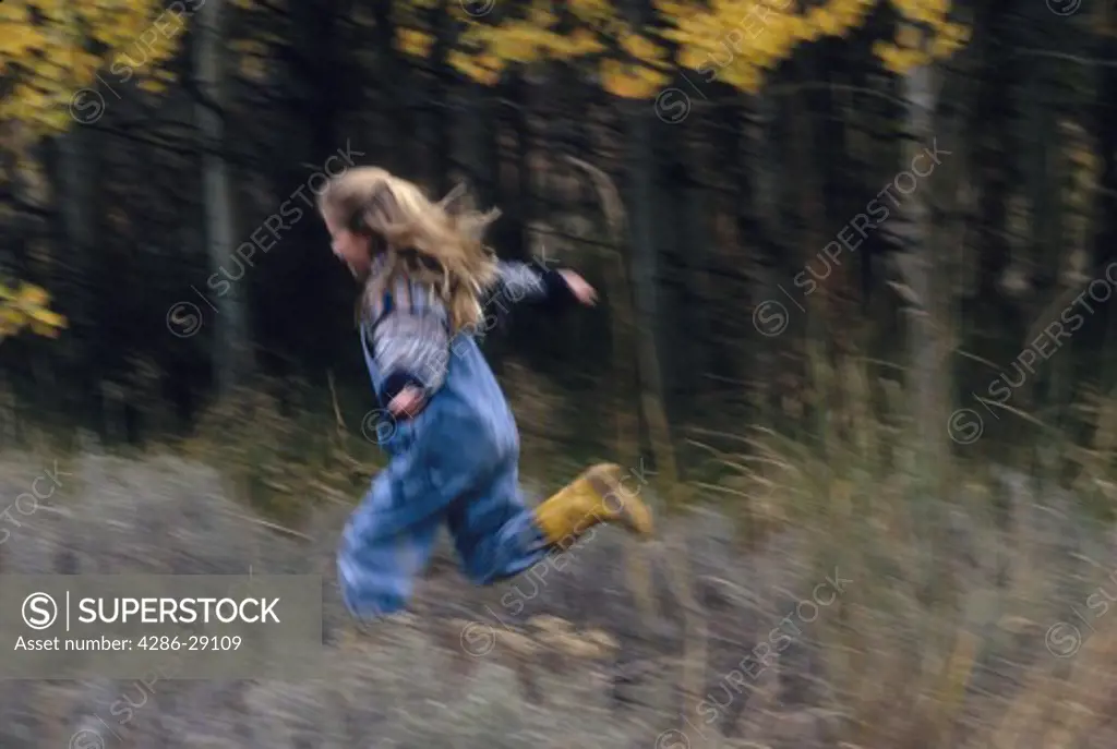 A young girl runs through a field by a woods.