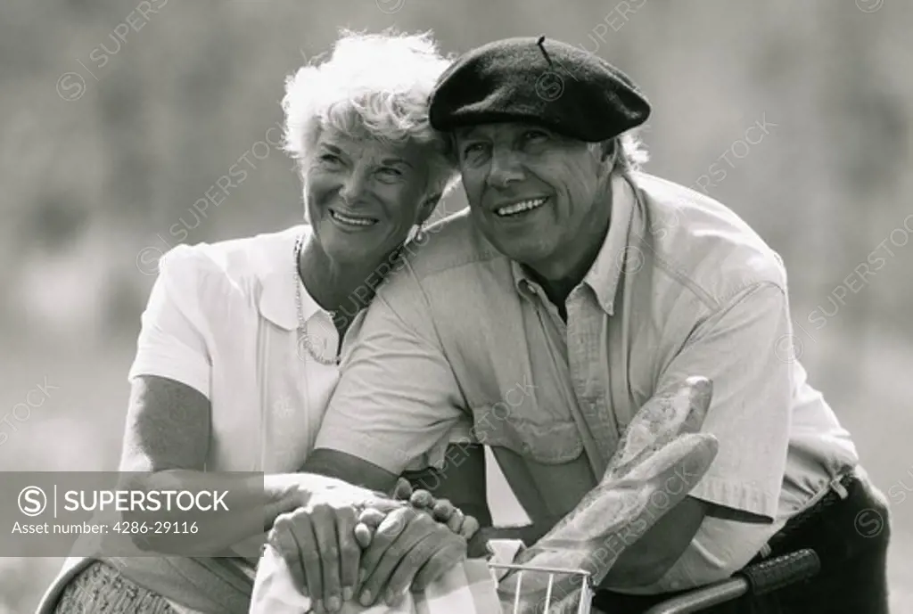 Happy mature couple lean on each other while outdoors on a picnic.