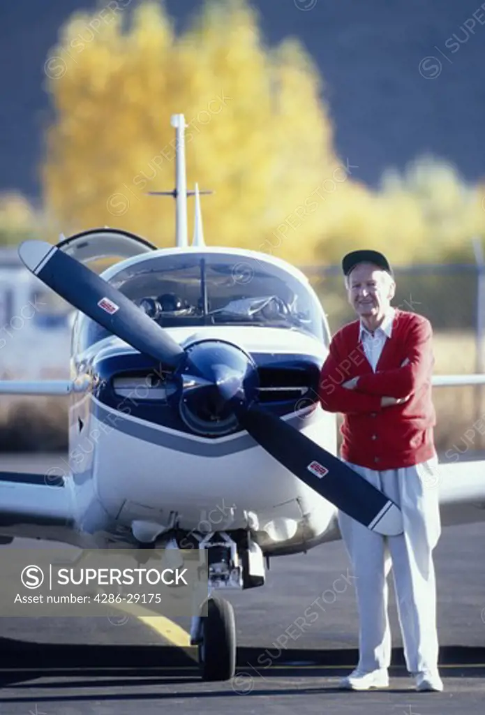 A smiling senior man stands confidently beside his single engine private plane.